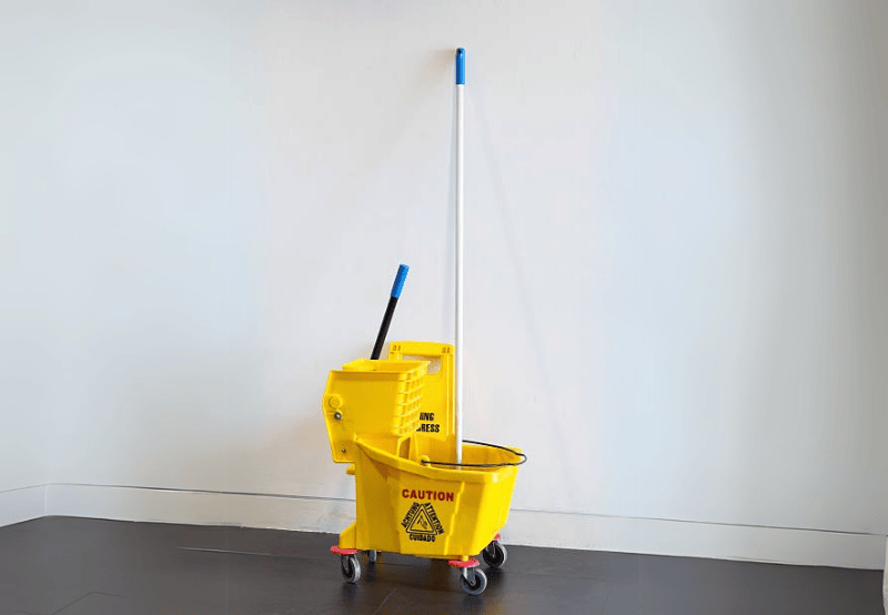 Yellow mop bucket with mop against white wall